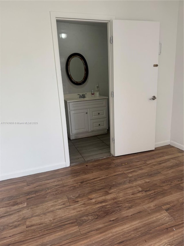 interior space with a sink, wood finished floors, baseboards, and connected bathroom