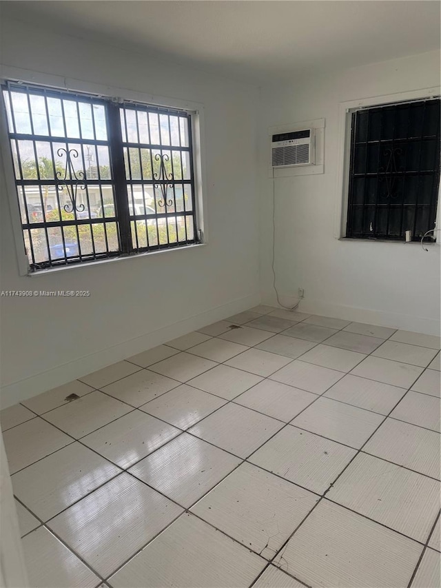 unfurnished room with tile patterned floors, an AC wall unit, and baseboards