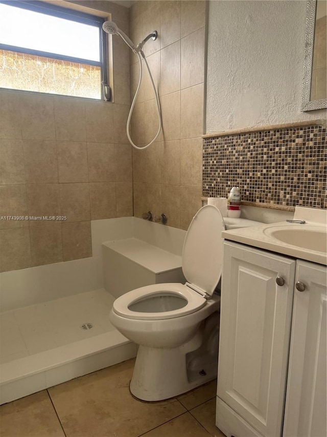 full bath with toilet, vanity, tiled shower, tile patterned floors, and tile walls