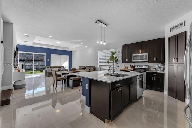 kitchen featuring decorative light fixtures, a center island with sink, stainless steel appliances, open floor plan, and a sink