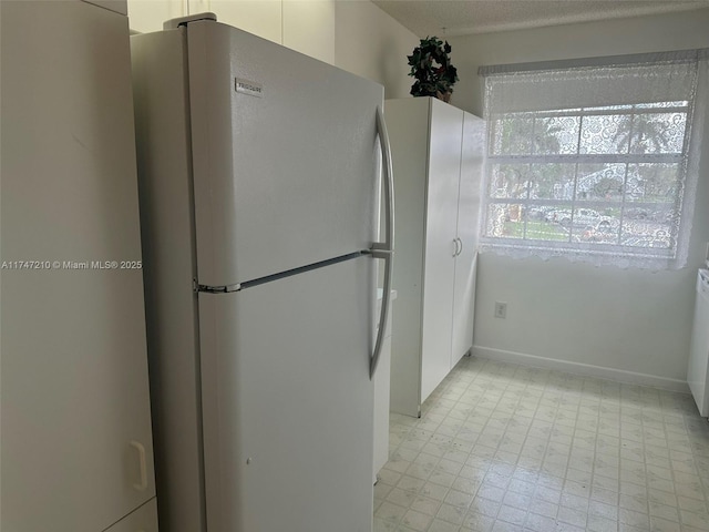 kitchen featuring light floors, baseboards, and freestanding refrigerator