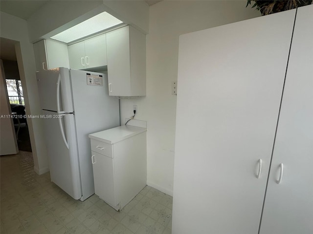 kitchen with baseboards, freestanding refrigerator, white cabinetry, light floors, and light countertops