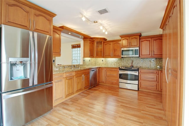 kitchen with a sink, visible vents, light wood-style floors, appliances with stainless steel finishes, and brown cabinetry