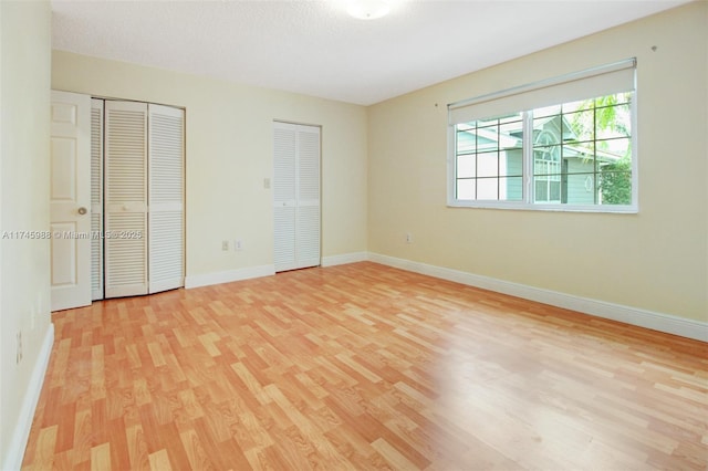 unfurnished bedroom with light wood-type flooring, a textured ceiling, baseboards, and two closets