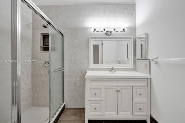 bathroom with tile walls, vanity, an enclosed shower, and wood-type flooring