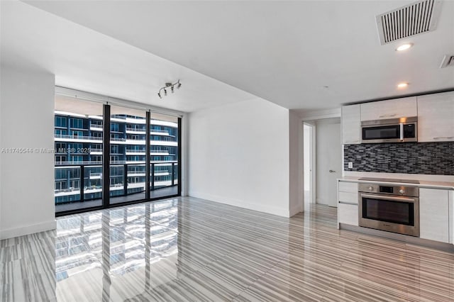 kitchen featuring white cabinets, appliances with stainless steel finishes, expansive windows, and tasteful backsplash