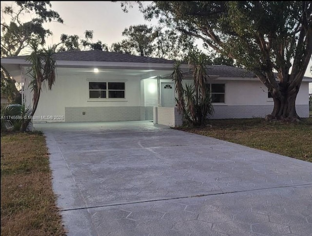 ranch-style house featuring driveway, stucco siding, roof with shingles, and brick siding