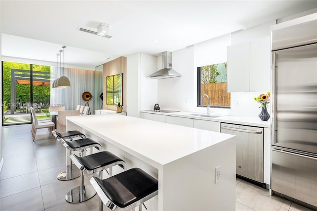 kitchen featuring sink, a center island, white cabinetry, wall chimney range hood, and stainless steel appliances