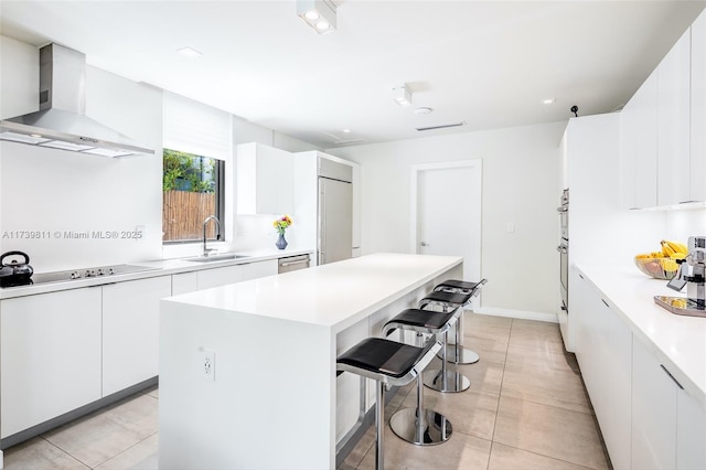 kitchen with white cabinetry, a center island, a breakfast bar, sink, and wall chimney exhaust hood