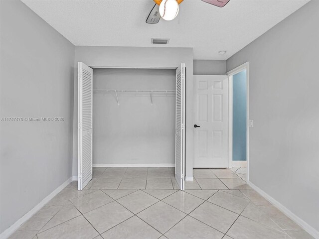 unfurnished bedroom with a textured ceiling, a closet, ceiling fan, and light tile patterned floors