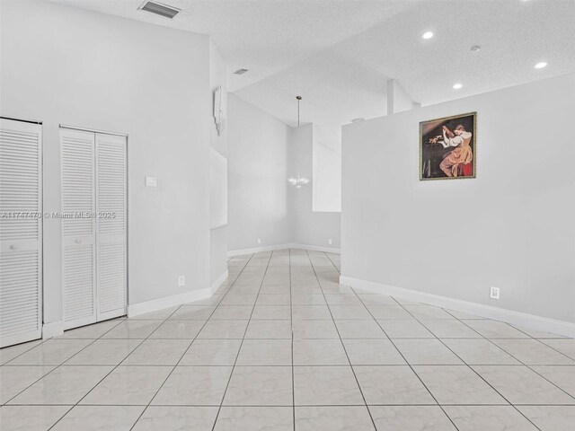 tiled spare room with a textured ceiling, high vaulted ceiling, and a chandelier