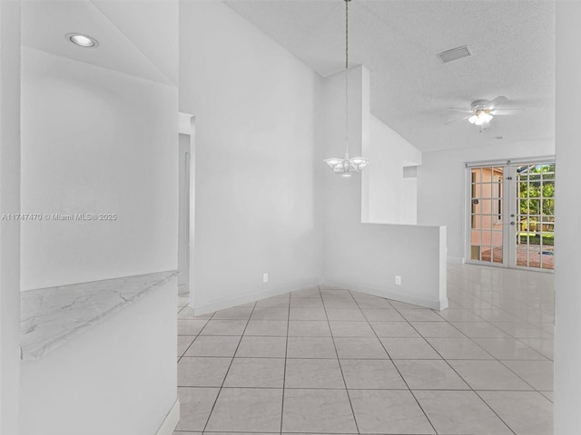 empty room with ceiling fan with notable chandelier, light tile patterned flooring, vaulted ceiling, and a textured ceiling