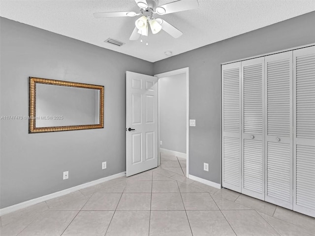 unfurnished bedroom featuring a textured ceiling, a closet, ceiling fan, and light tile patterned floors