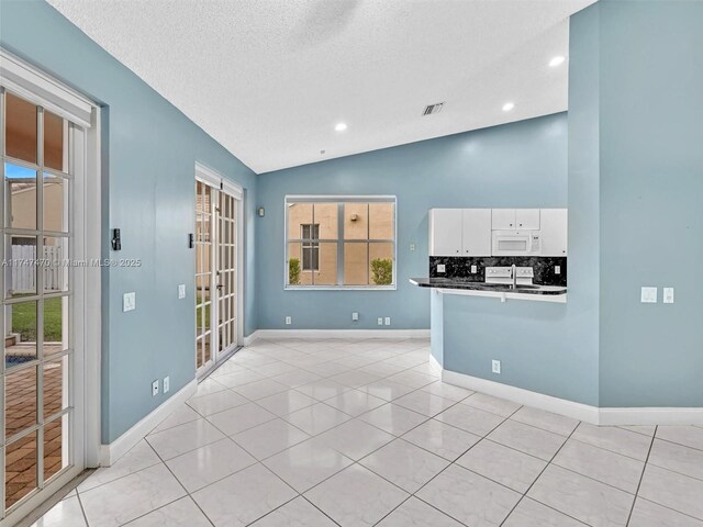 unfurnished room featuring vaulted ceiling, a textured ceiling, and light tile patterned floors