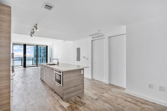 kitchen with electric panel, sink, a water view, a wall of windows, and an island with sink