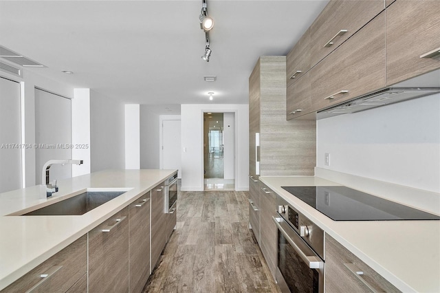 kitchen featuring sink, rail lighting, oven, light hardwood / wood-style floors, and black electric stovetop