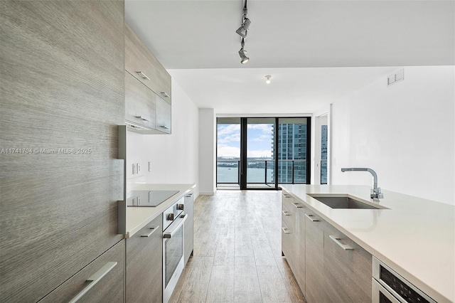 kitchen featuring stainless steel oven, a water view, sink, a wall of windows, and black electric stovetop