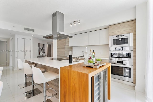 kitchen featuring visible vents, modern cabinets, island exhaust hood, black electric cooktop, and a kitchen bar