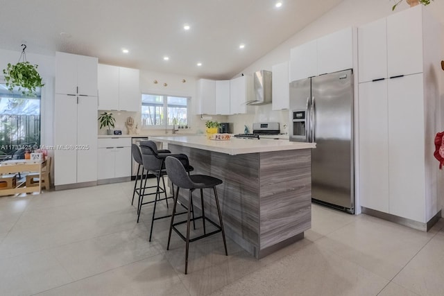 kitchen with a kitchen bar, a kitchen island, stainless steel appliances, wall chimney exhaust hood, and white cabinets