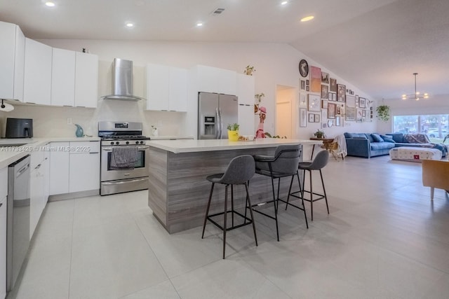 kitchen featuring stainless steel appliances, a breakfast bar, a kitchen island, white cabinets, and wall chimney range hood