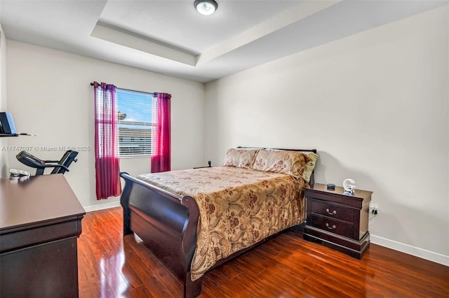 bedroom with a raised ceiling and dark hardwood / wood-style floors