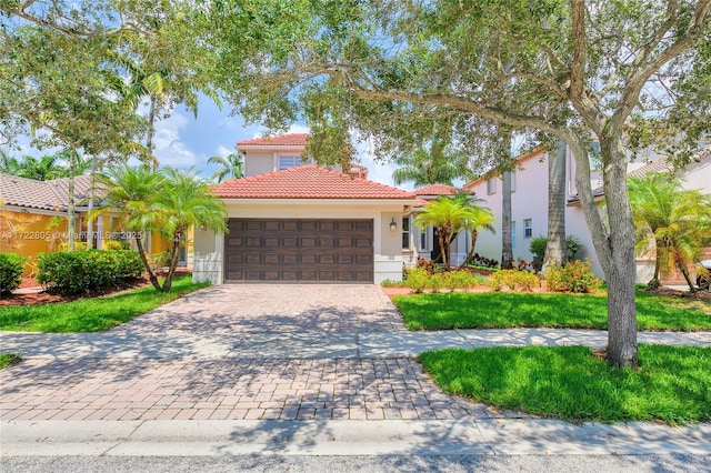 mediterranean / spanish home featuring a garage, decorative driveway, a tile roof, and stucco siding