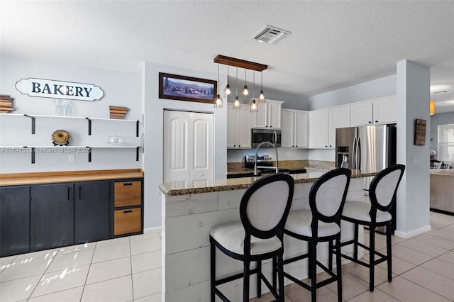 kitchen featuring light tile patterned floors, a breakfast bar area, appliances with stainless steel finishes, and visible vents