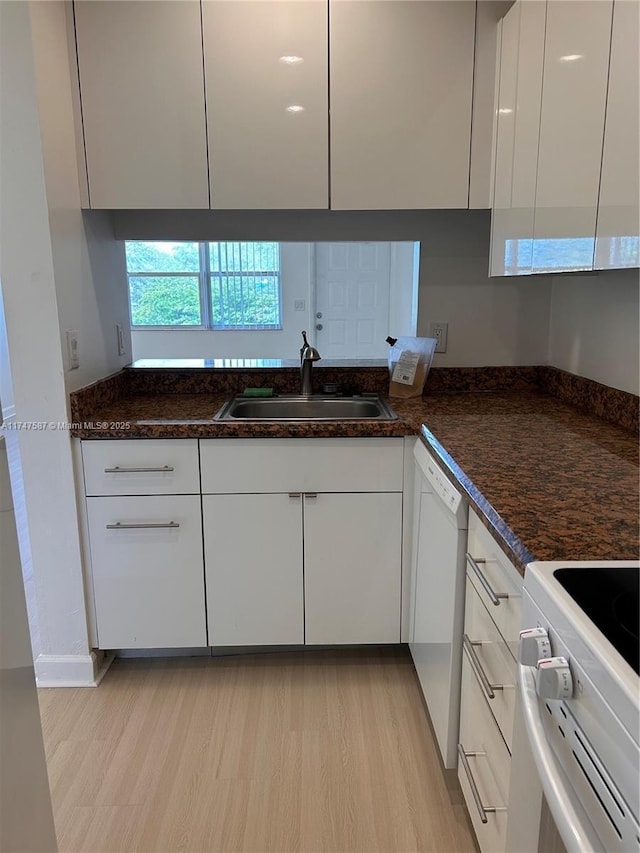 kitchen featuring white appliances, light hardwood / wood-style flooring, sink, white cabinetry, and dark stone counters