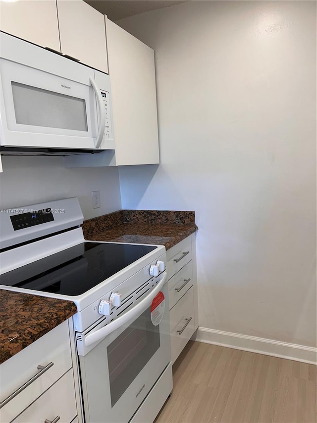 kitchen with dark stone countertops, white appliances, white cabinets, and light hardwood / wood-style floors