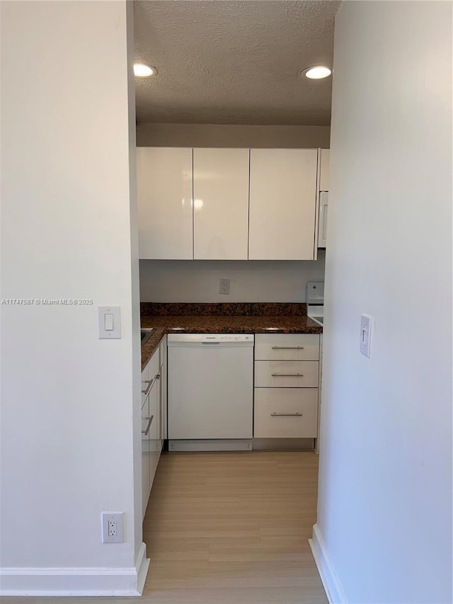 kitchen featuring light hardwood / wood-style flooring, white cabinetry, dishwasher, dark stone counters, and a textured ceiling