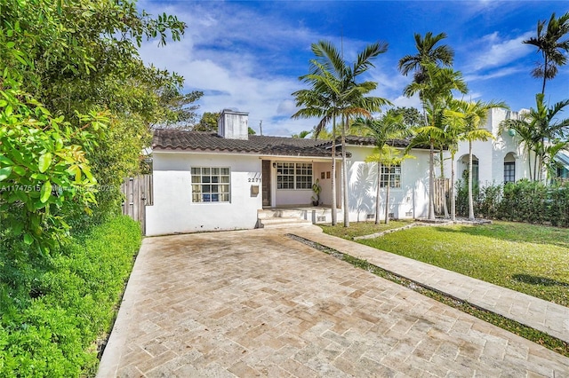 view of front of home with a tiled roof, a chimney, a front lawn, and stucco siding