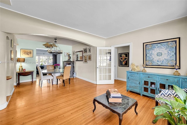 living area featuring arched walkways, an inviting chandelier, light wood-style flooring, and baseboards