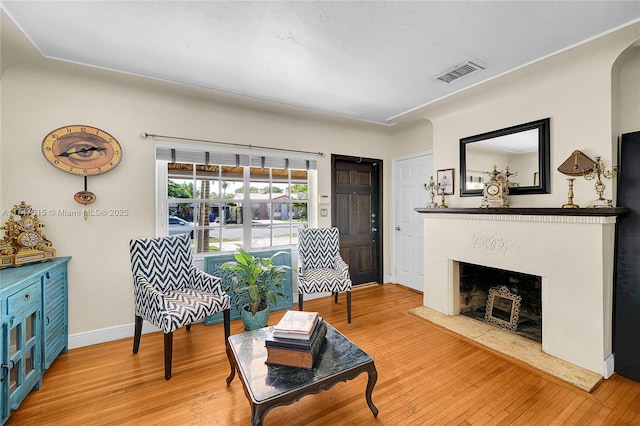 living room featuring a fireplace with raised hearth, light wood-style flooring, visible vents, and baseboards