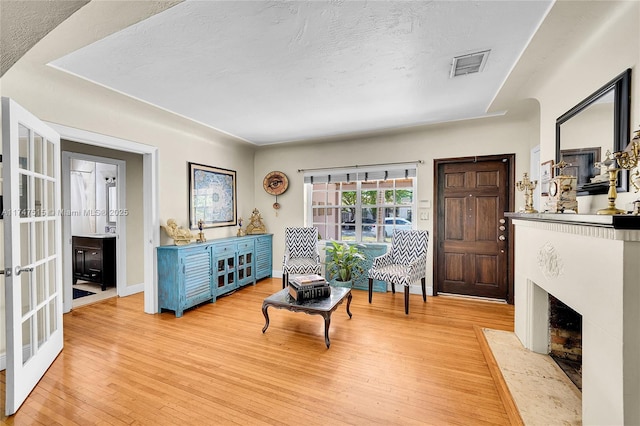 sitting room featuring french doors, visible vents, a textured ceiling, light wood-type flooring, and baseboards