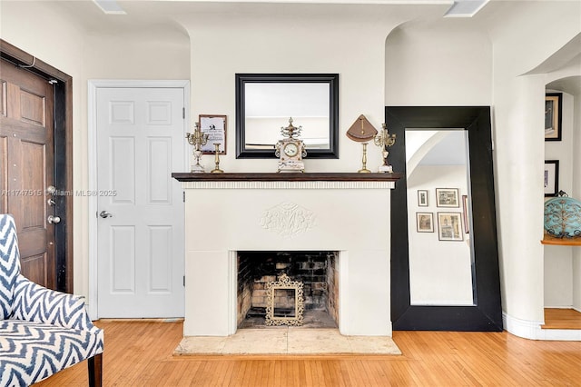 living room featuring a fireplace with raised hearth, arched walkways, and wood finished floors