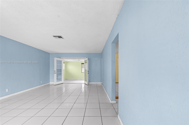 tiled empty room featuring a textured ceiling and french doors