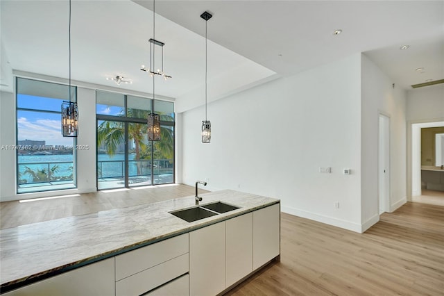 kitchen with white cabinetry, light hardwood / wood-style floors, sink, light stone counters, and pendant lighting