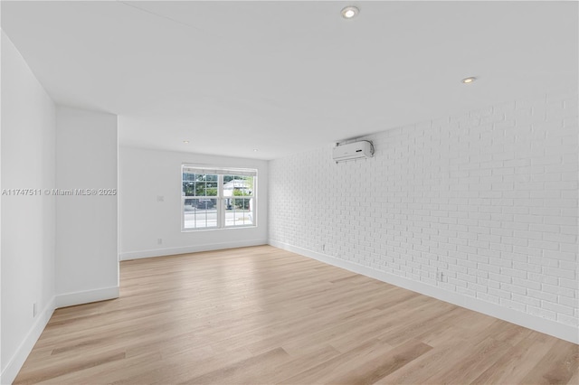 empty room featuring light hardwood / wood-style flooring, brick wall, and a wall mounted air conditioner