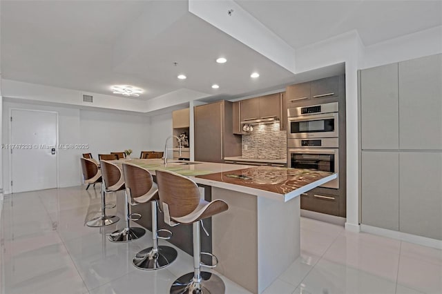 7825 NW 107th Ave Unit 618, Doral, FL 33178 - kitchen with sink, a kitchen breakfast bar, stainless steel double oven, an island with sink, and tasteful backsplash