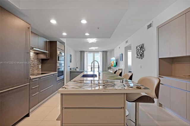 7825 NW 107th Ave Unit 618, Doral, FL 33178 - kitchen with a center island with sink, sink, tasteful backsplash, light tile patterned floors, and a kitchen breakfast bar
