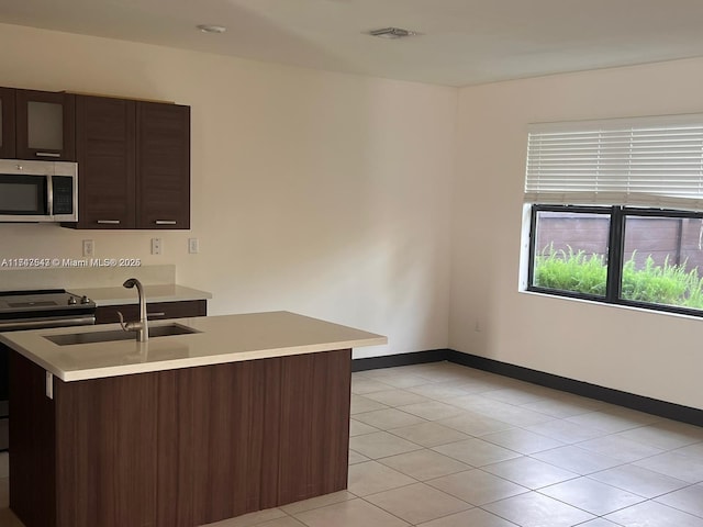 kitchen featuring appliances with stainless steel finishes, sink, light tile patterned floors, kitchen peninsula, and dark brown cabinets