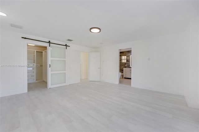 unfurnished bedroom with light hardwood / wood-style flooring, a walk in closet, and a barn door