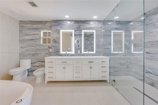 bathroom with a shower with door, toilet, tile walls, vanity, and a bidet