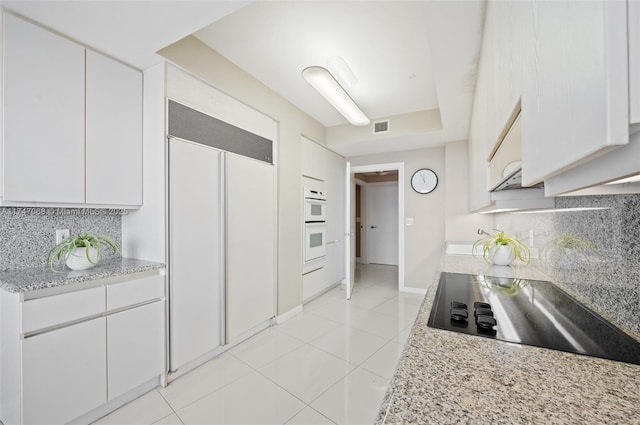 kitchen featuring light stone countertops, paneled built in fridge, white cabinets, black electric cooktop, and decorative backsplash