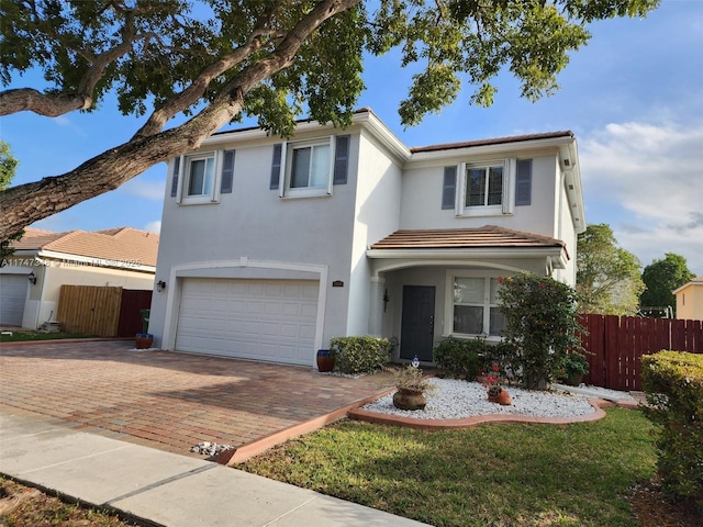 traditional-style home with decorative driveway, fence, an attached garage, and stucco siding