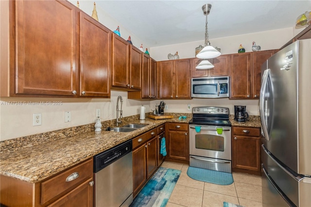 kitchen featuring light tile patterned floors, dark stone countertops, hanging light fixtures, stainless steel appliances, and a sink