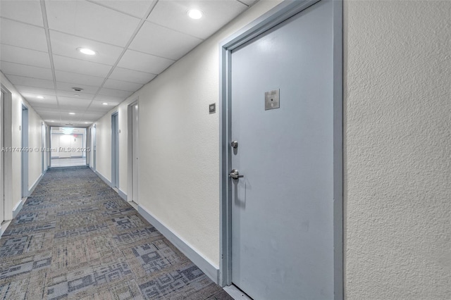 hall featuring dark colored carpet and a drop ceiling