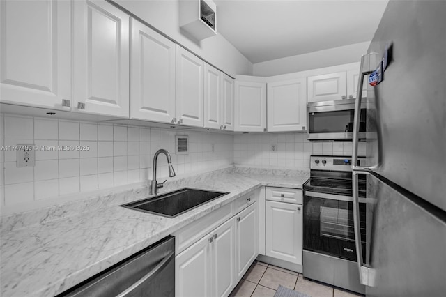 kitchen featuring appliances with stainless steel finishes, sink, light tile patterned floors, light stone counters, and white cabinetry