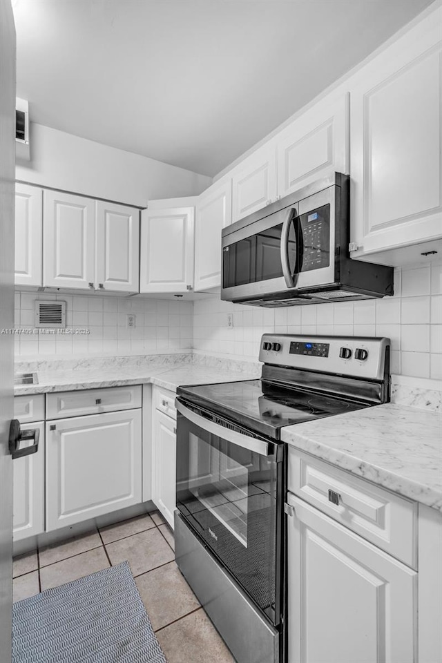 kitchen with appliances with stainless steel finishes, light tile patterned floors, white cabinetry, light stone countertops, and tasteful backsplash