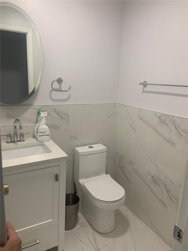 bathroom with toilet, a wainscoted wall, vanity, tile walls, and marble finish floor